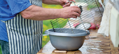 Man scrubbing a grill grate over a bowl of water