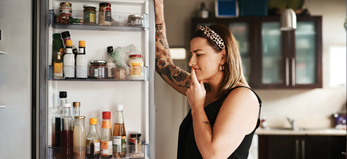 Woman holding fridge door open and thinking