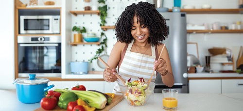 Happy woman mixing up a salad in the kitchen