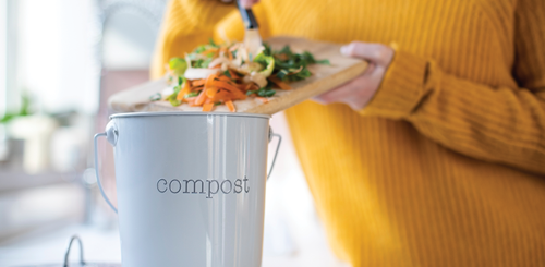 Person pushing food scraps from a cutting board into a compost bucket