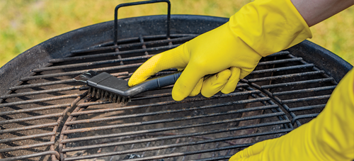 Close up of hands wearing cleaning gloves, scrubbing a grill with a grill brush